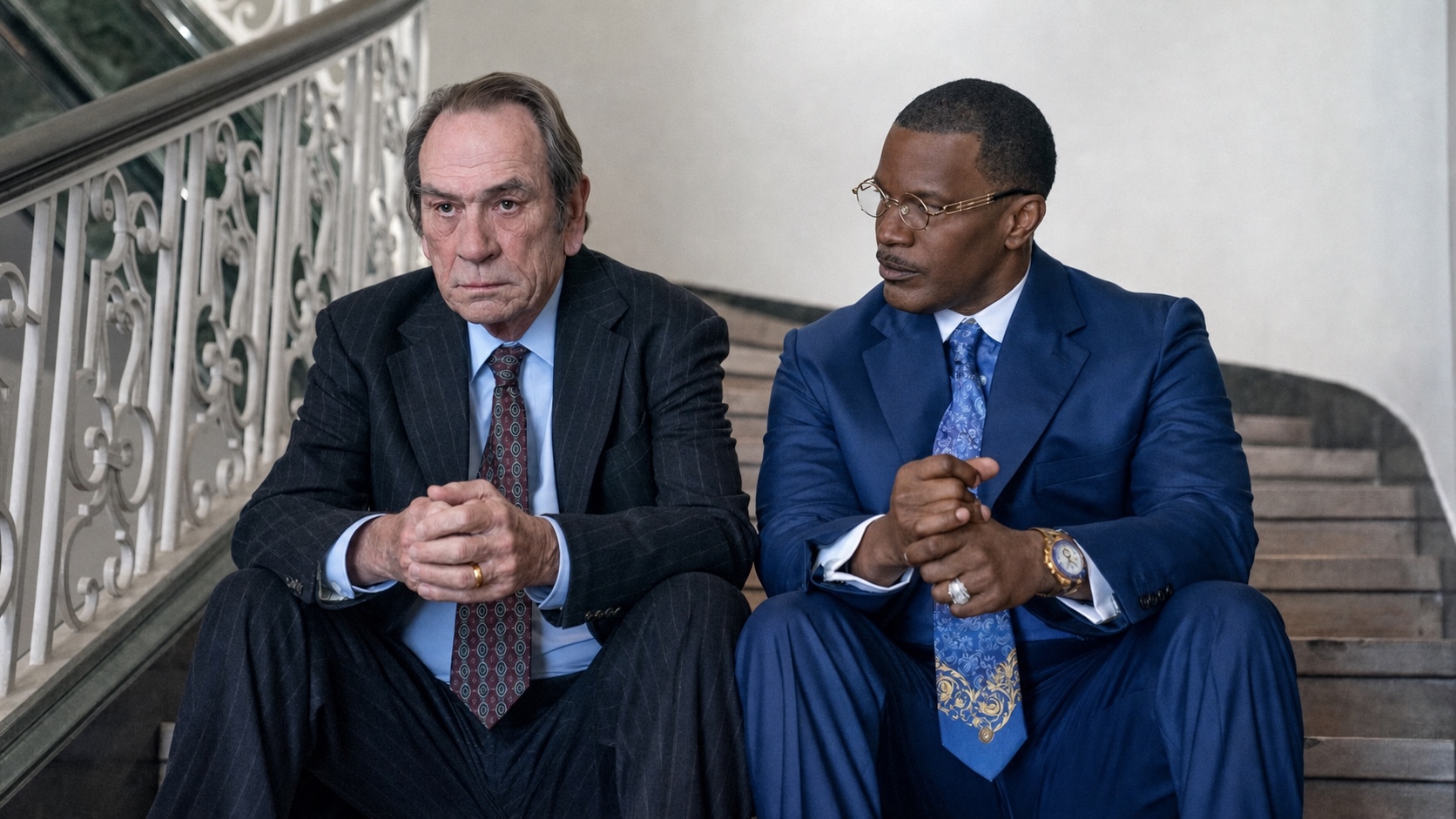 Jamie Foxx in a blue suit and Tommy Lee Jones in pinstripes seated on a staircase, The Burial
